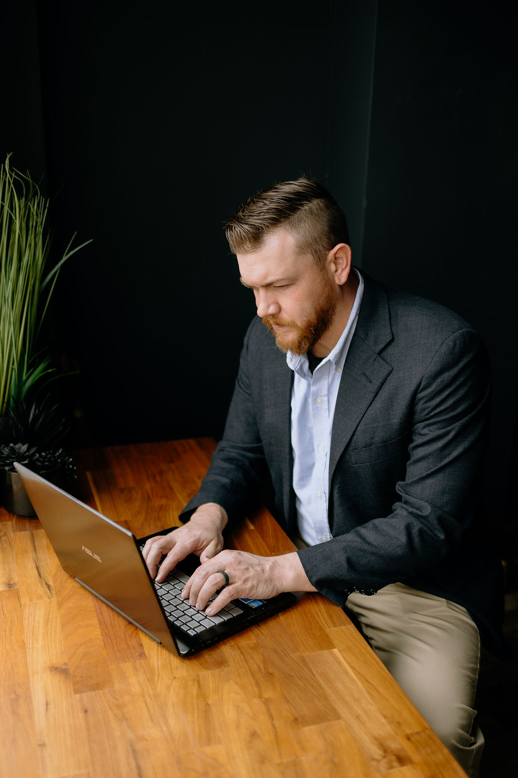 Joshua Schafer working at a laptop on a wooden table, dressed in a navy blazer, focused on his screen